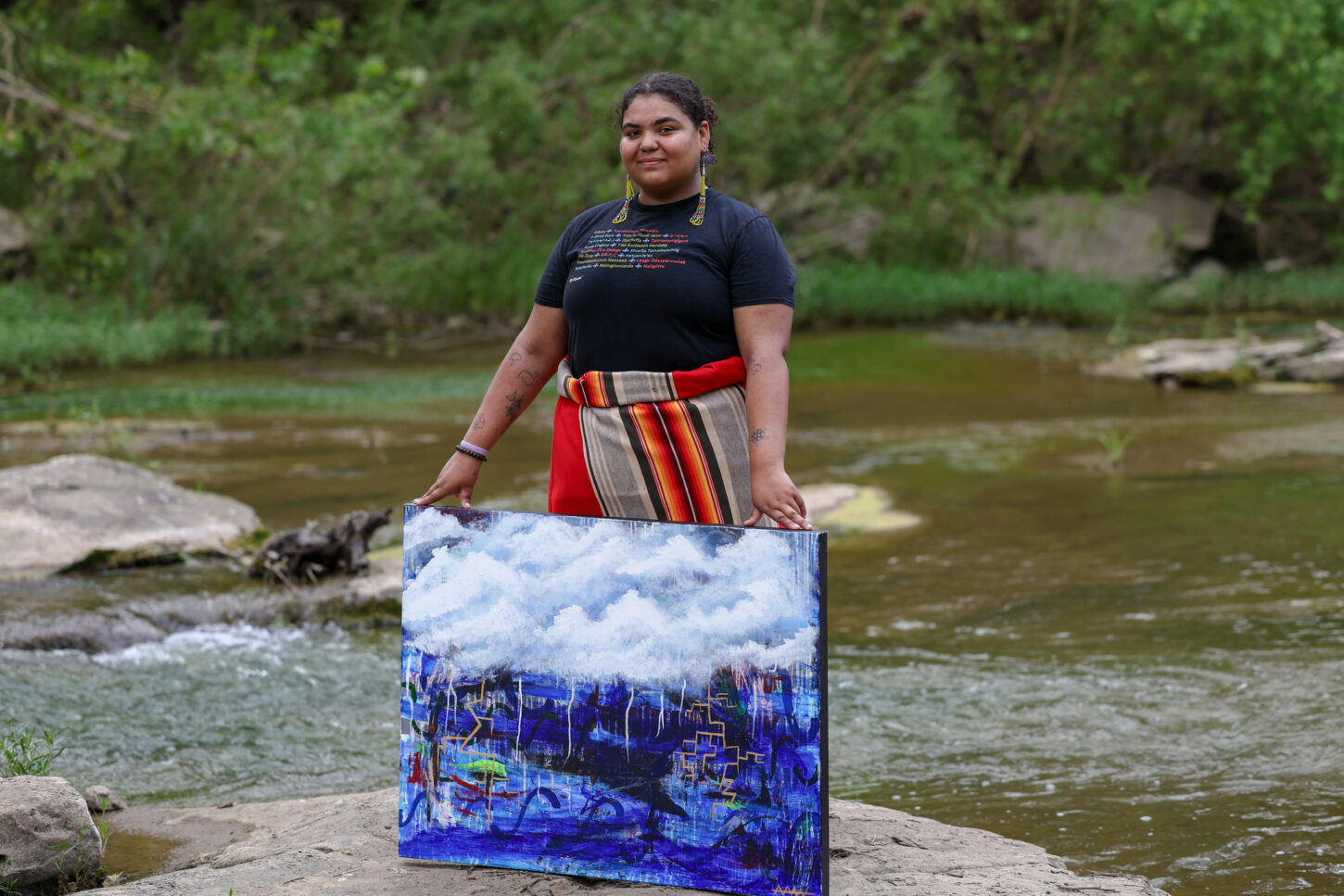 A woman holds a painting by a waterway