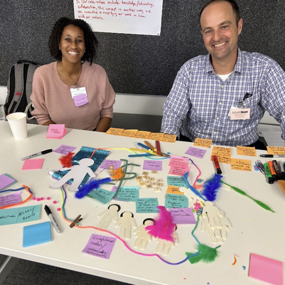 Two Beacon Cohort participants sit at a table covered in sticky notes and pens