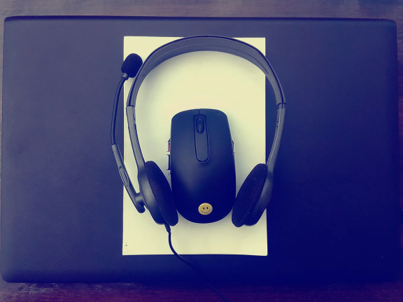 Headphones, a laptop, and a computer mouse sit on a desk