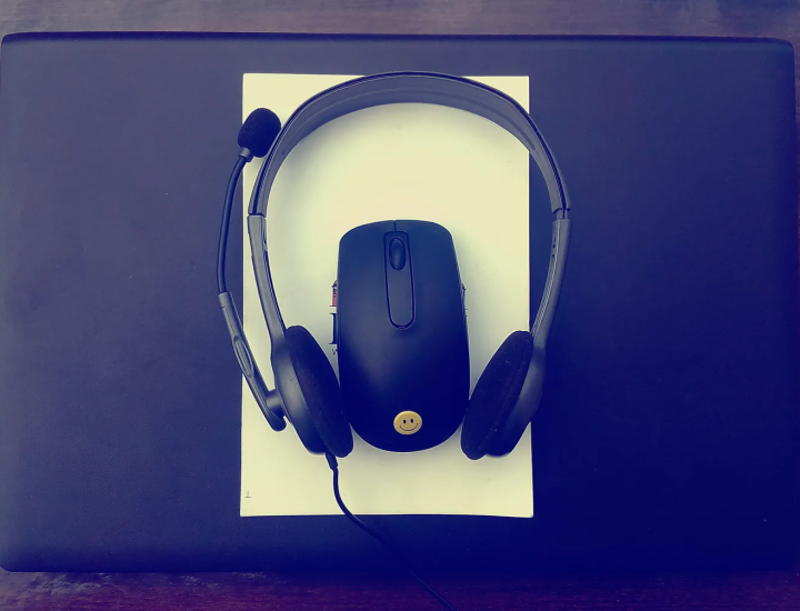 Headphones, a laptop, and a computer mouse sit on a desk