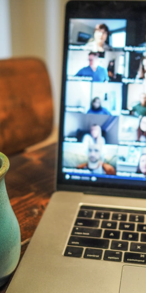 A coffee mug rests on a table next to a laptop screen showing a virtual meeting in progress